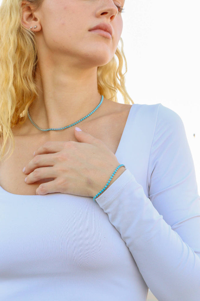 Woman wearing a light blue top with a turquoise necklace against a white background