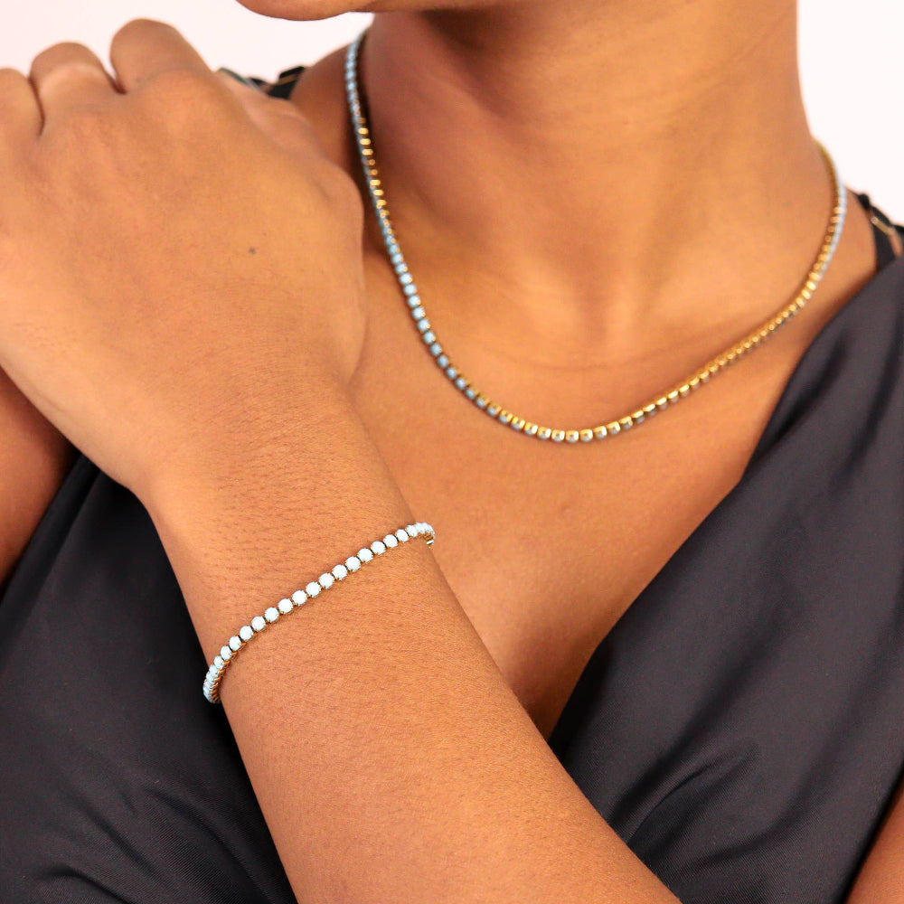 Person wearing a gold necklace and silver bracelet on a plain background