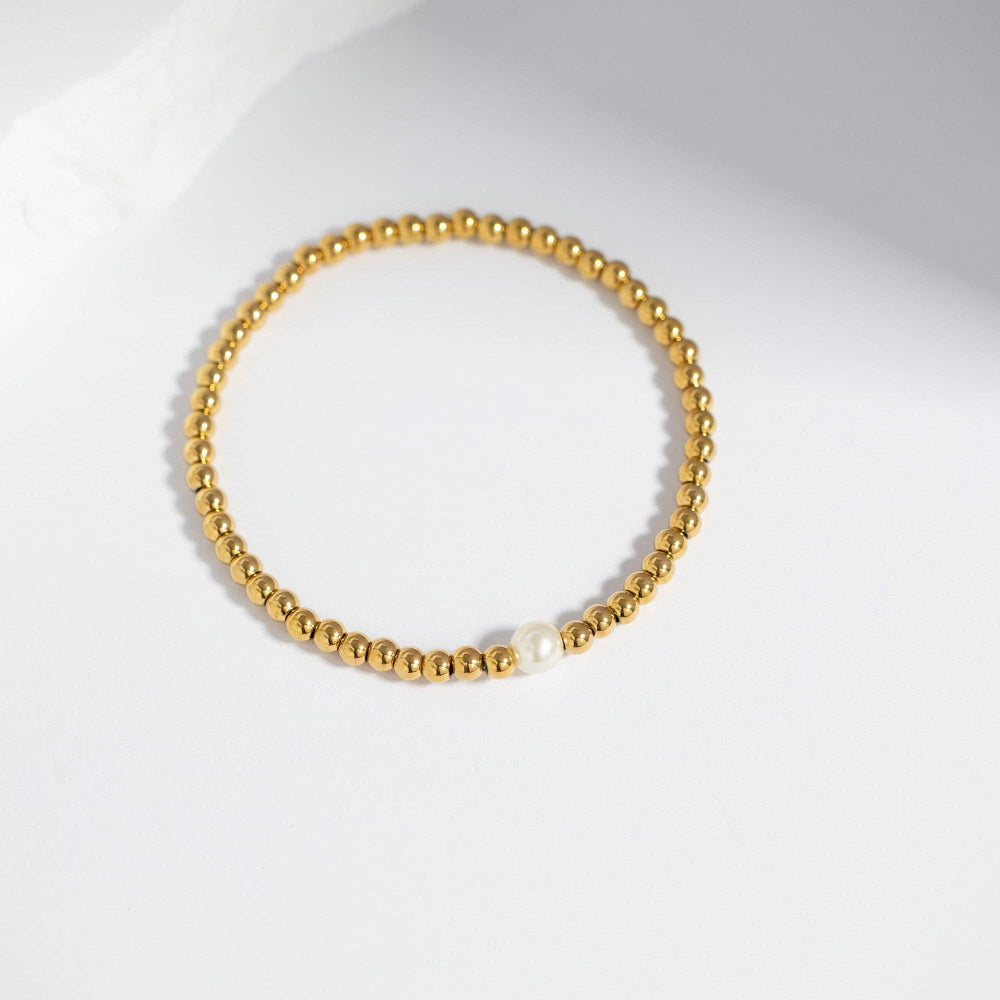 Gold beaded bracelet with a pearl on a white background