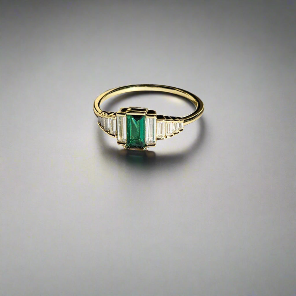 Gold ring with a green gemstone on a light surface, branded 'Hollyberg Jewels'.
