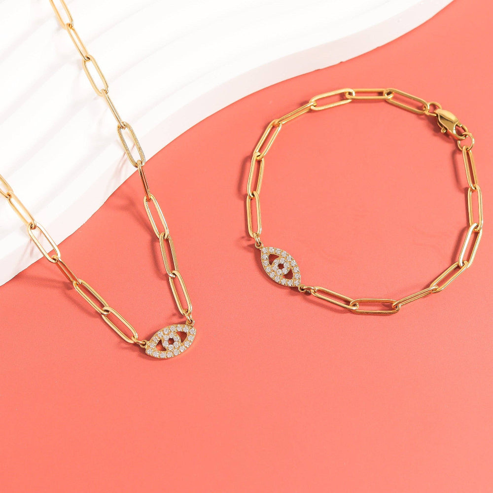 Gold chain necklace and bracelet with eye design on a pink background