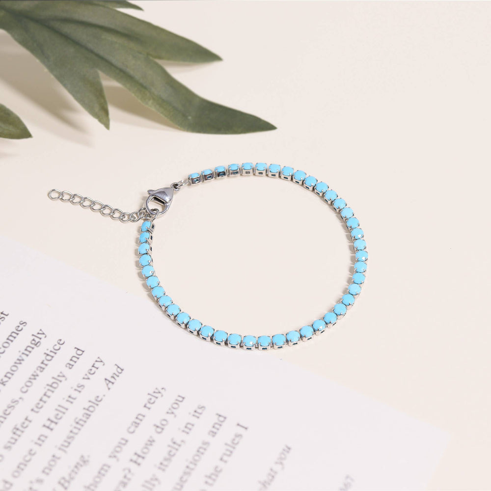 Turquoise beaded bracelet on a white surface with green leaves in the background