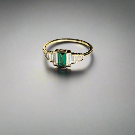 Gold ring with a green gemstone on a light surface, branded 'Hollyberg Jewels'.